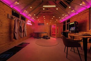 A room with a wooden interior, a massage table, a massage chair, a gaming table, and a neon sign. - Historic Clocktower House | Spa Barn | Sleeps 12 (Cumberland)
