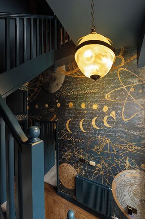 A staircase with a dark blue railing, a hanging light fixture, and a wall with astronomical and scientific illustrations. - Historic Clocktower House | Spa Barn | Sleeps 12 (Cumberland)