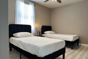 Un dormitorio con dos camas individuales, un ventilador de techo y una ventana con cortinas.