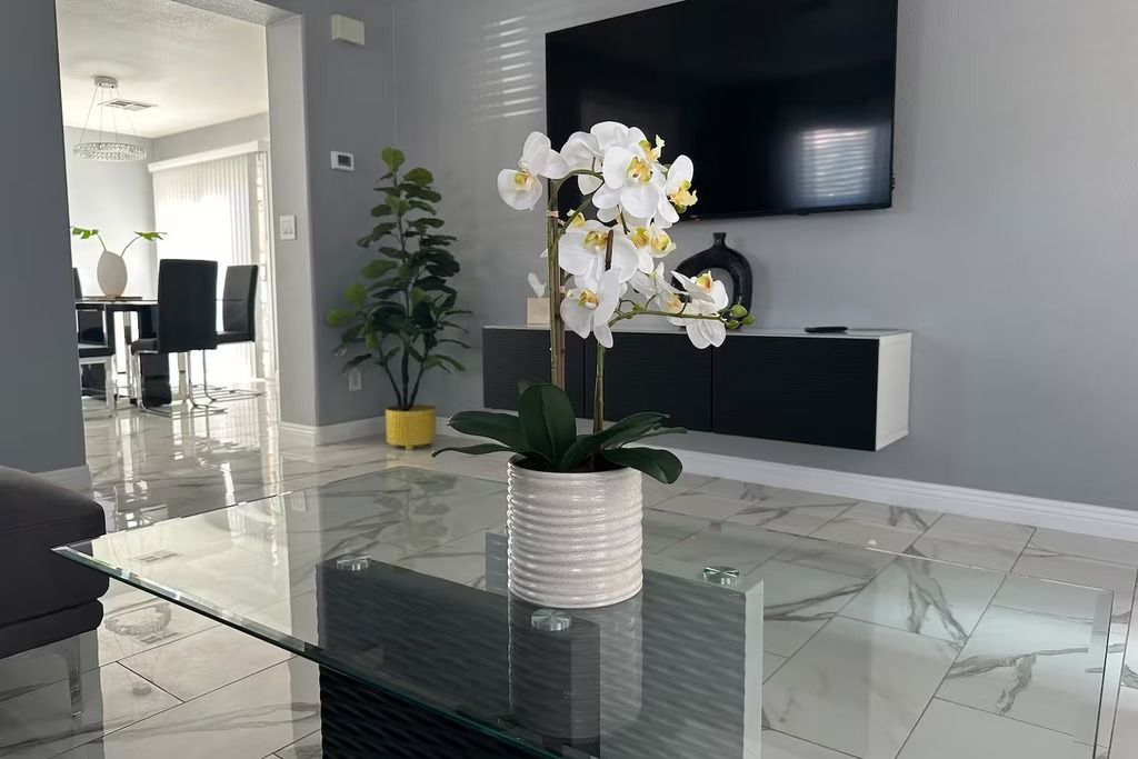 Een moderne woonkamer met een glazen salontafel, een potorkidee, een flatscreen televisie en een minimalistische entertainmentsunit.