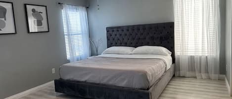 Une chambre à coucher avec un lit, un ventilateur de plafond et deux fenêtres avec des rideaux.