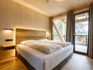 Ein Schlafzimmer mit einem Holzkopfteil, einem Bett mit weißer Bettwäsche, einem Nachttisch und einem großen Fenster mit Vorhängen.