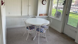 Una habitación con una mesa y sillas blancas, un reloj en la pared y vistas al exterior.