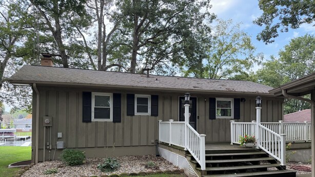 A two-story house with a front porch, a small garden, and a dock in the background.