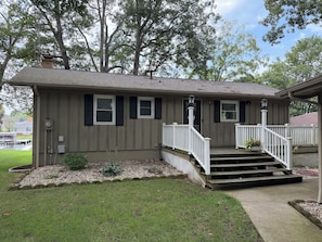 A two-story house with a front porch, a small garden, and a dock in the background.