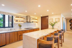 Una cocina moderna con encimera de mármol, armarios de madera, estufa integrada y una barra con taburetes.