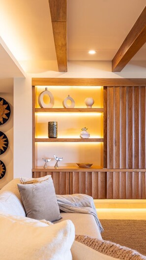 Una sala de estar moderna con una pared de madera decorativa, un estante empotrado con adornos y una zona de estar acogedora con cojines.