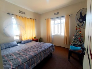 Un dormitori amb un llit, cortines, una finestra, un ventilador i un arbre de Nadal.