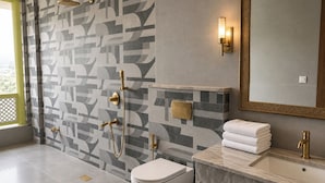A modern bathroom with a geometric patterned wall, a toilet, a sink with a marble countertop, and a shower with gold fixtures. - juSTa Luxe Monsoon Palace (Udaipur)
