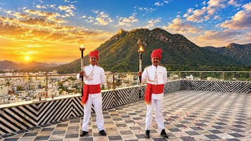 Dos personas sosteniendo antorchas en una azotea, con un paisaje urbano y montañas al fondo.