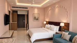 A hotel room with a bed, a sofa, a round table, a TV, and a ceiling fan. - juSTa Luxe Monsoon Palace (Udaipur)