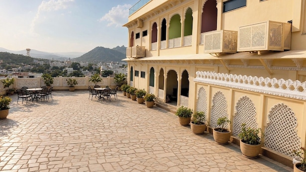 A courtyard with a tiled floor, potted plants, outdoor seating, and a view of a cityscape and mountains in the distance. - juSTa Luxe Monsoon Palace (Udaipur)