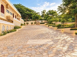 Un patio con un sendero de piedra que lleva a un edificio con ventanas arqueadas y un balcón.