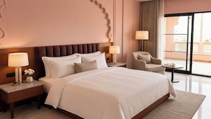 A hotel room with a large bed, two bedside tables with lamps, a chair, and a view through a large window. - juSTa Luxe Monsoon Palace (Udaipur)
