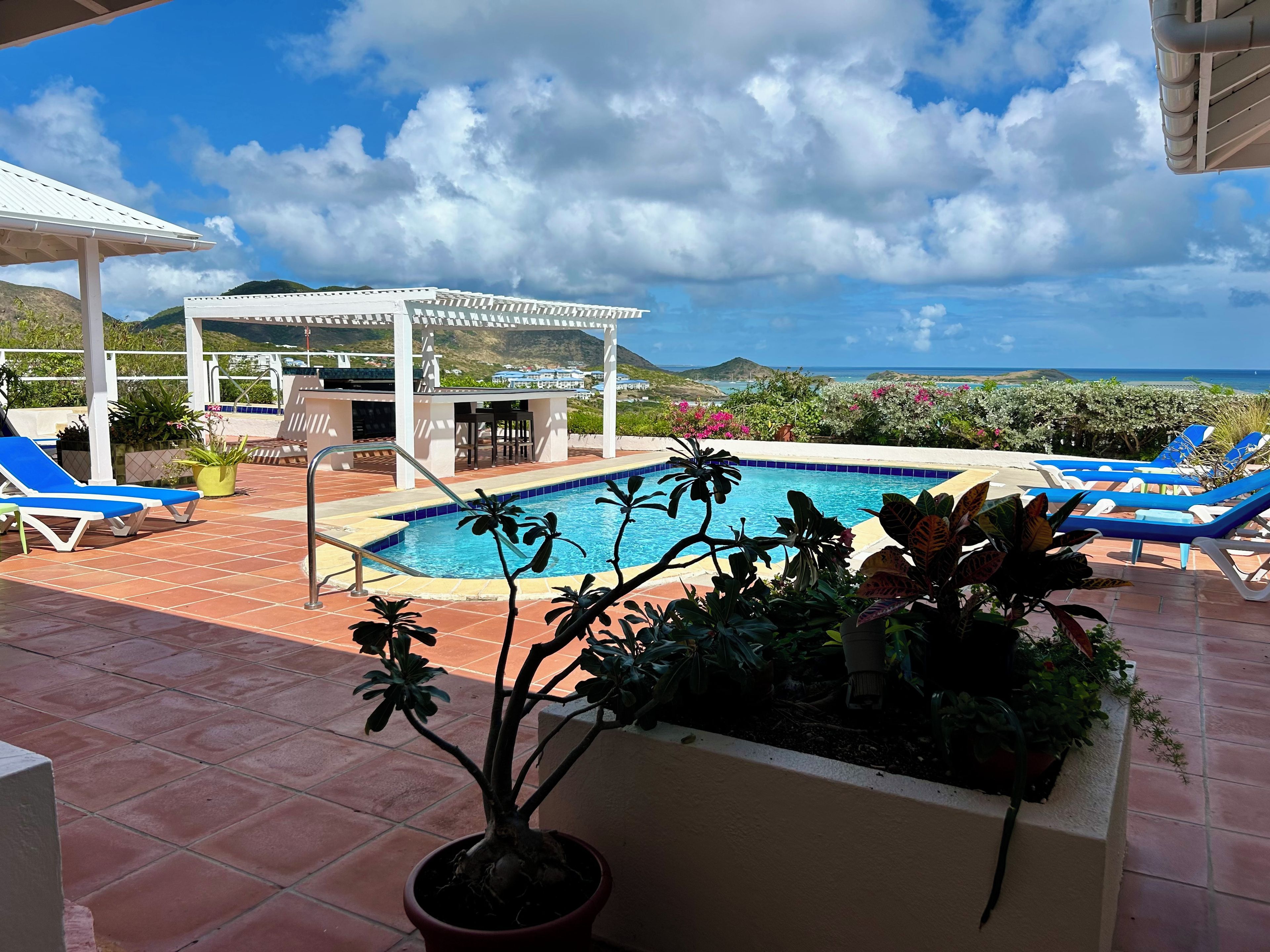 Area piscina con poltrone relax, una pergola e vista sull'oceano.