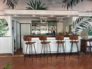 A bar area with a counter, stools, and a variety of bottles.
