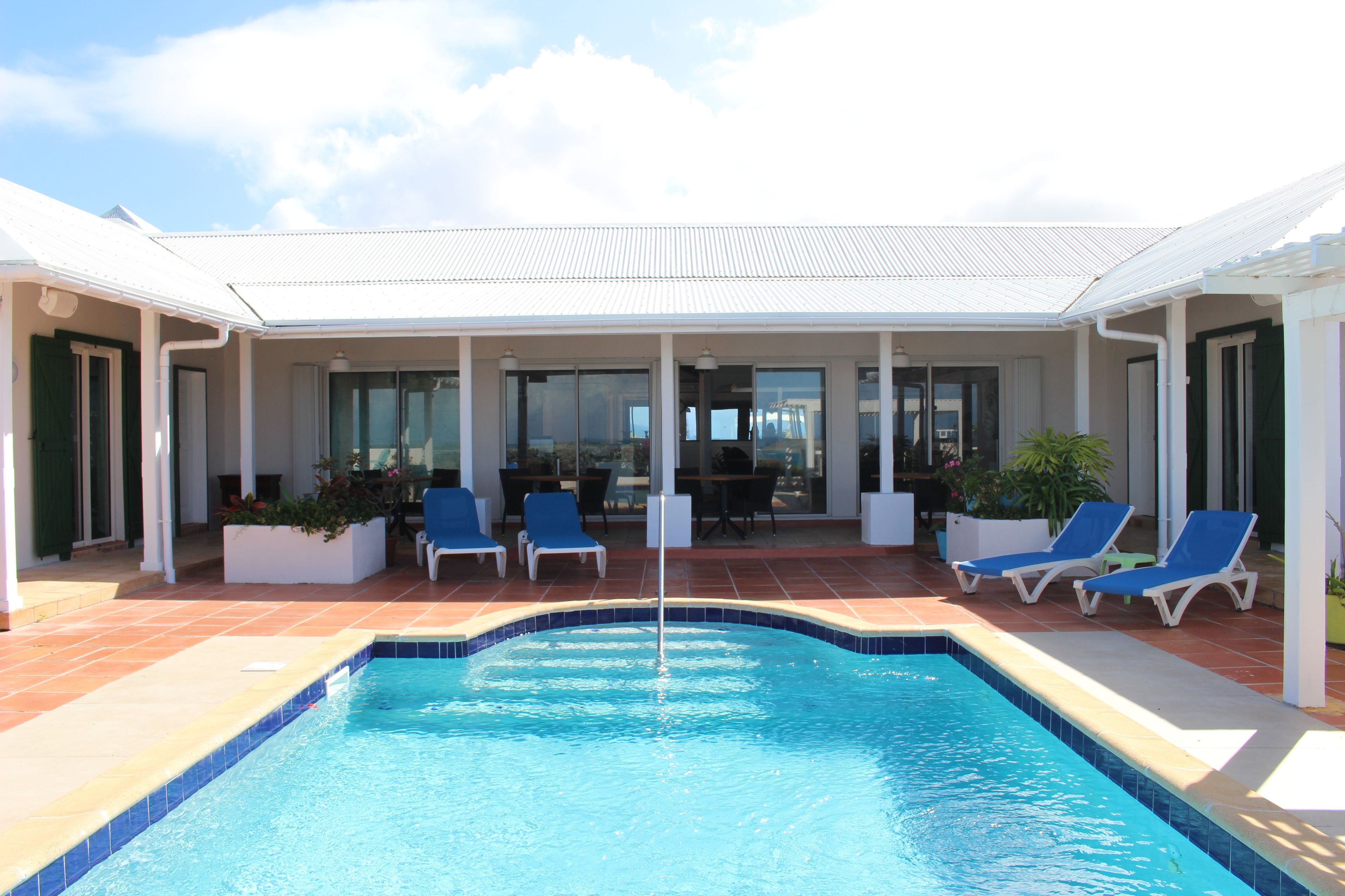 A pool area with a clear blue pool, surrounded by lounge chairs and potted plants.