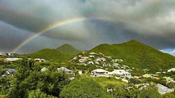 A residential area with houses on a hillside, a mountain in the background, and a rainbow.