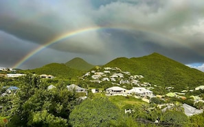 A residential area with houses on a hillside, a mountain in the background, and a rainbow.