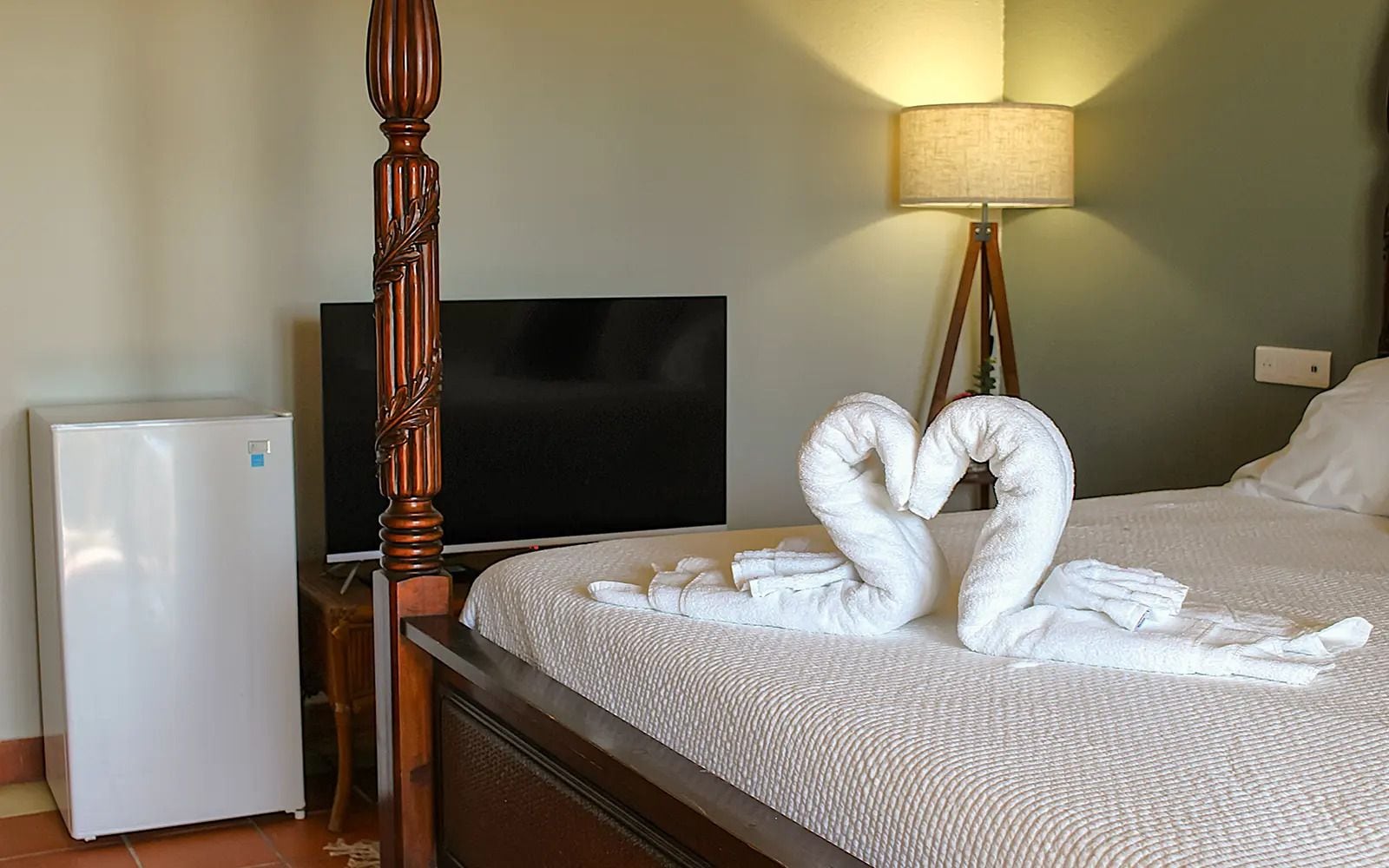 Una habitación de hotel con una cama, televisor, lámpara y refrigerador.