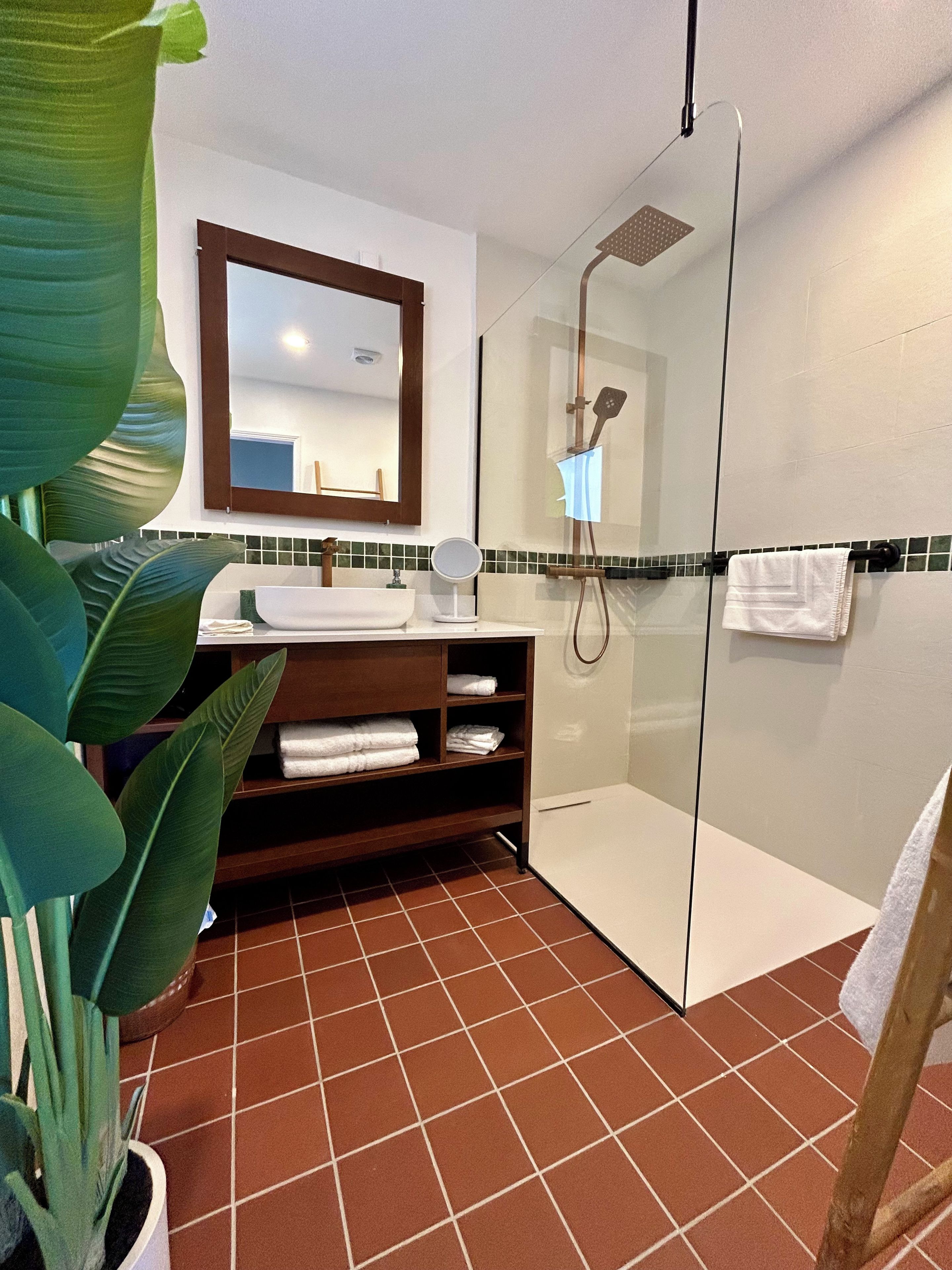 Un baño con cabina de ducha de vidrio, un lavamanos con espejo y un estante con toallas dobladas.