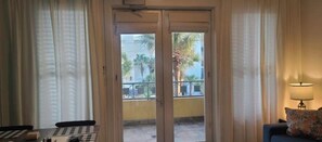 A room with a sliding glass door leading to a balcony with palm trees and a building in the background.