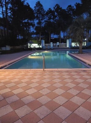 A swimming pool with a tiled deck, surrounded by trees and a fence.