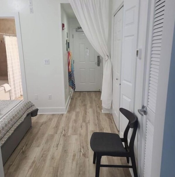 A narrow hallway with a bed, a chair, and a door leading to another room.