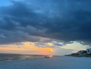 A beach with a sunset, a few people, and buildings in the background.