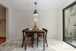 Un comedor con una mesa preparada para cuatro personas, una lámpara colgante y vista a un árbol a través de una puerta de cristal.