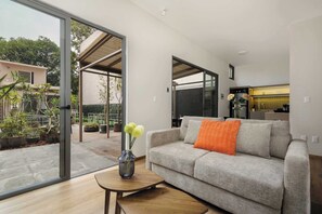A modern living room with a grey sofa, a small wooden table with a vase, and a glass door leading to an outdoor patio with potted plants. - Zaterra - House with Independent Apartments in Roma Norte (Ciudad de México)