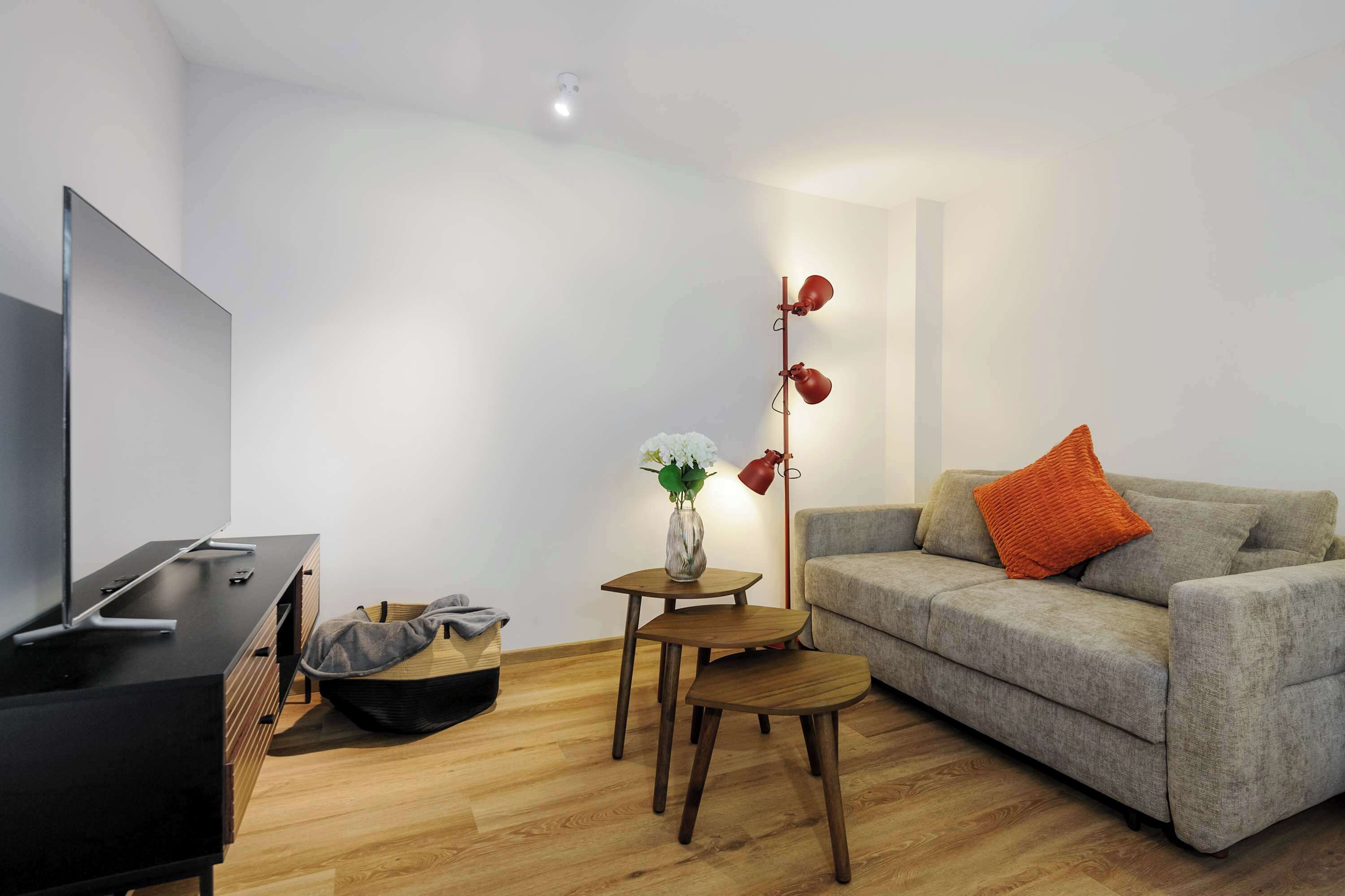 A modern living room with a grey sofa, a small wooden table, a TV stand, and a floor lamp.