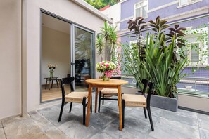 Eine Terrasse mit einem runden Tisch und vier Stühlen, umgeben von Blumentöpfen und einer Glastür zu einem Innenbereich.