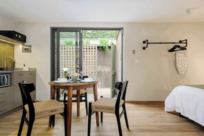 A compact room with a dining table, two chairs, a bed, and a view of a garden through a glass door. - Zaterra - House with Independent Apartments in Roma Norte (Ciudad de México)