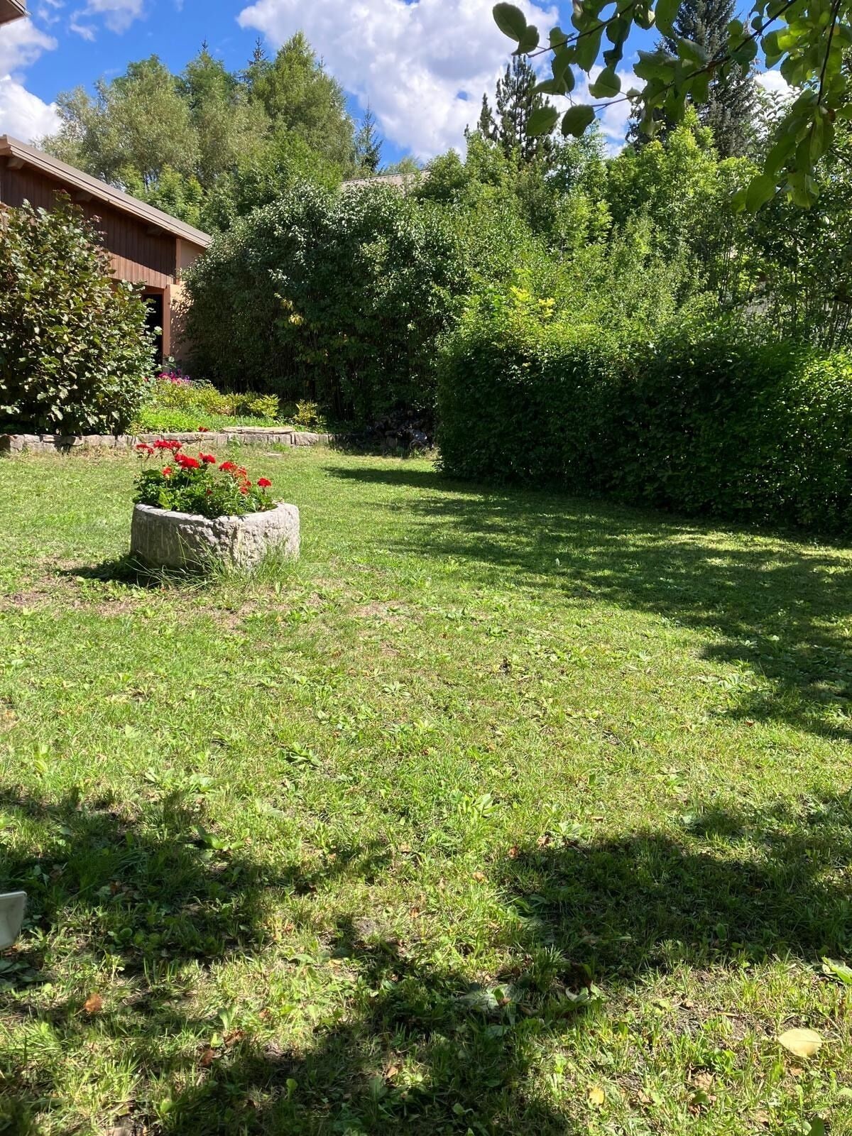 A well-maintained garden with a stone planter, lush green grass, and a variety of trees and shrubs.