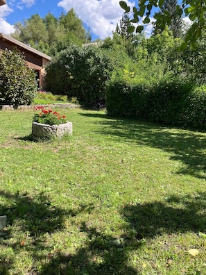 Un jardin bien entretenu, agrémenté d’un jardinière en pierre, d’une pelouse verdoyante et d’une variété d’arbres et d’arbustes.