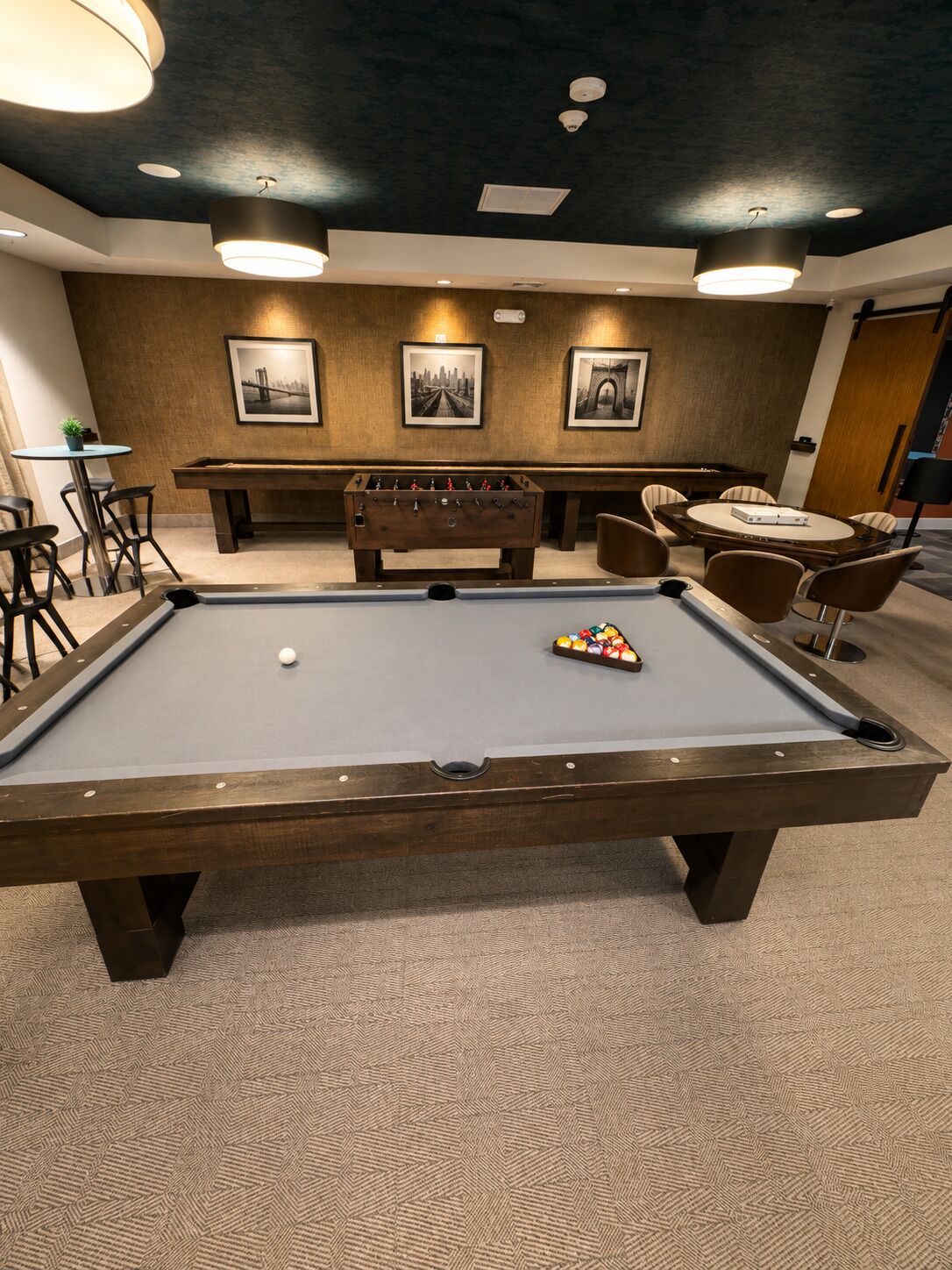 Uma mesa de bilhar com bola branca e um conjunto de bolas coloridas, cercada por cadeiras e uma mesa de futebol de botão.