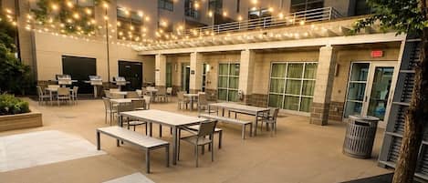 An outdoor patio area with tables and chairs, string lights, and a building entrance.