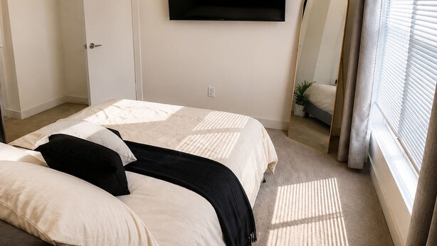 Een slaapkamer met een bed, een flatscreen televisie, een spiegel en een raam met zonwering.