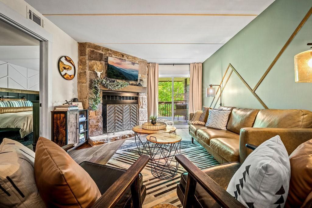 A living room with a stone fireplace, leather sofas, and a view of greenery outside.