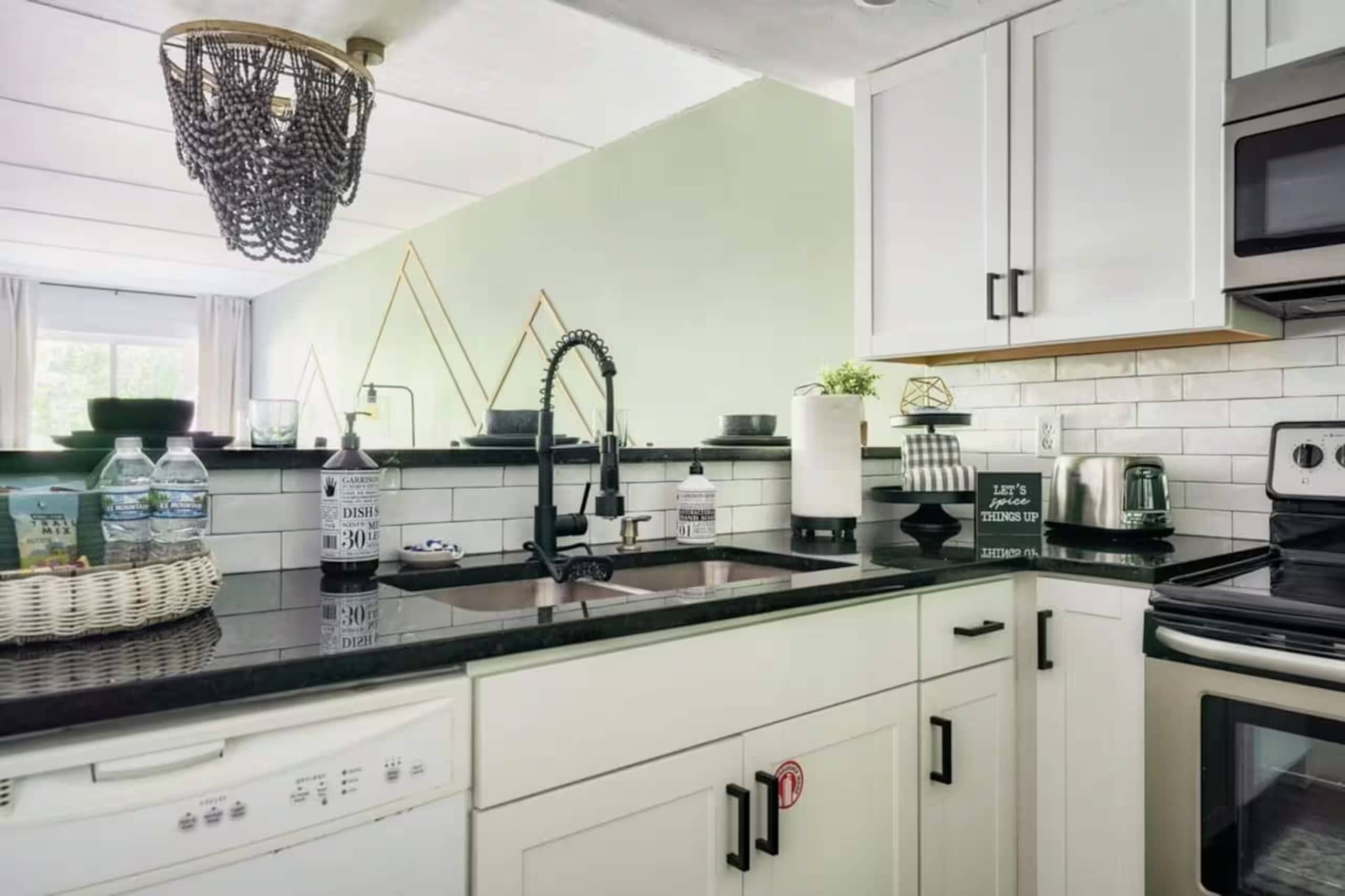 Una cucina moderna con mobili bianchi, un piano di lavoro nero, un piano cottura in acciaio inossidabile e un lampadario.