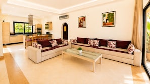 A modern living room with a sectional sofa, a glass coffee table, and a dining area with a wooden table and chairs.