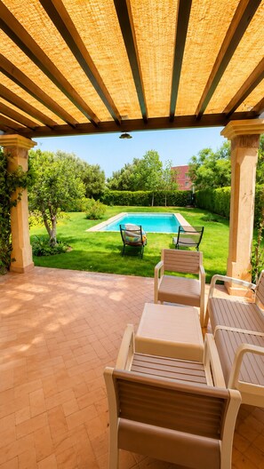 An outdoor patio with a pool, chairs, and a view of a garden.