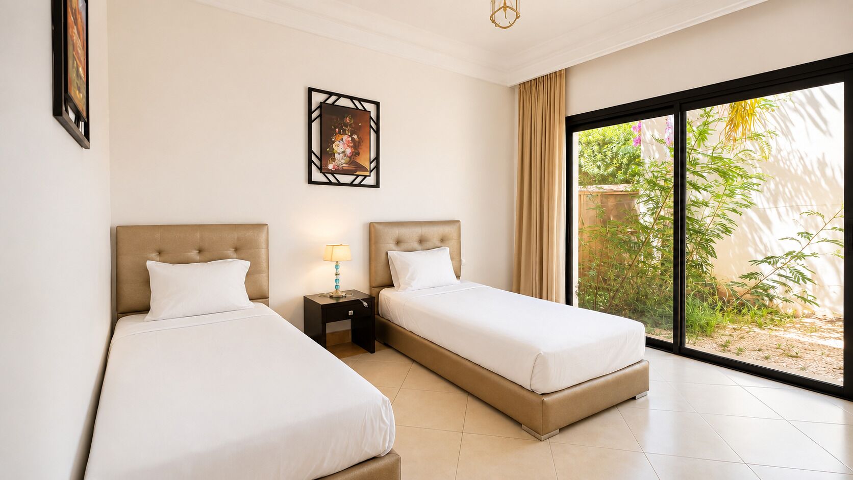 Une chambre d’hôtel avec deux lits, une table de chevet avec une lampe, un tableau encadré au mur et une grande fenêtre donnant sur un paysage verdoyant.