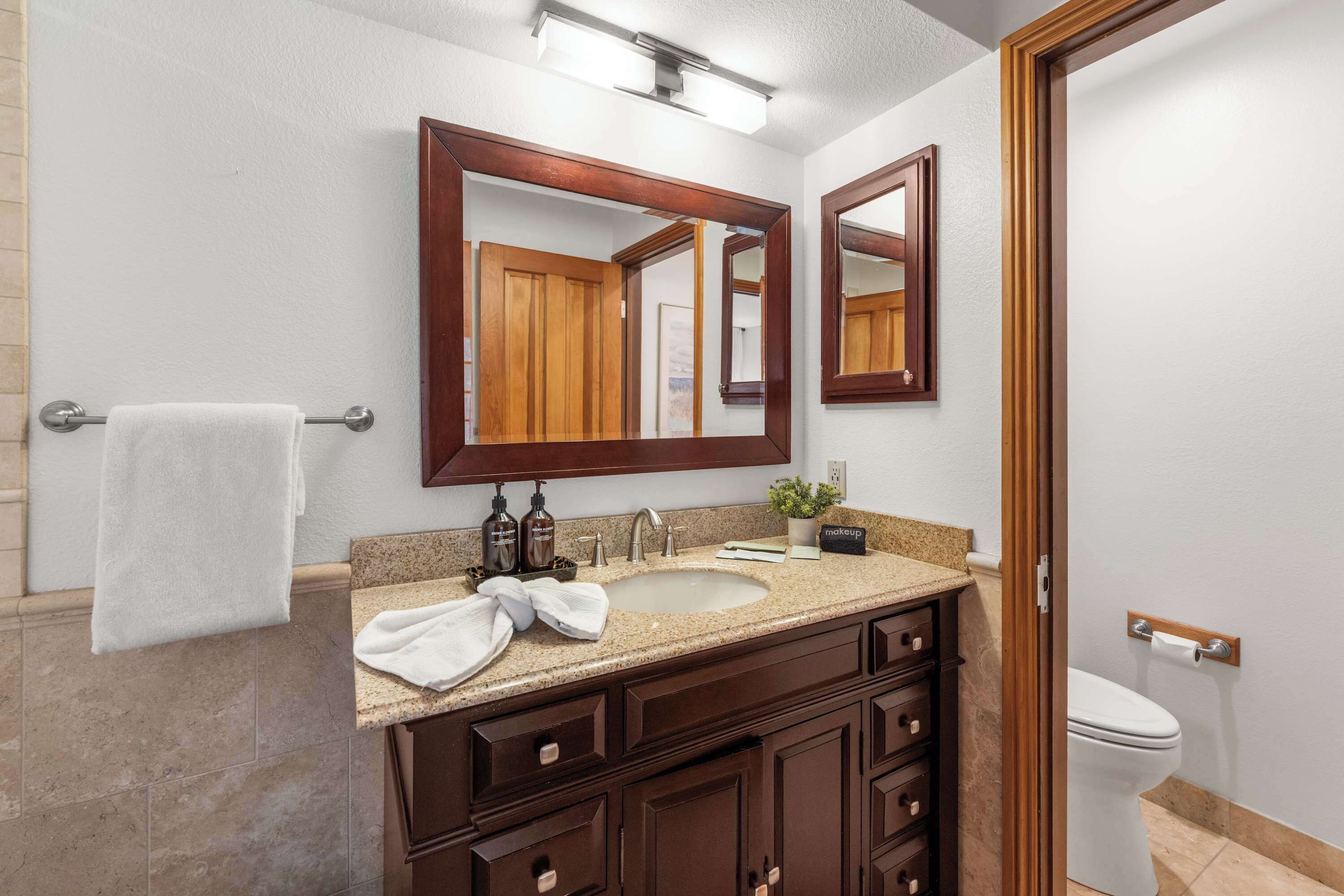A bathroom with a double vanity, a large mirror, a towel rack, a sink, and a toilet.