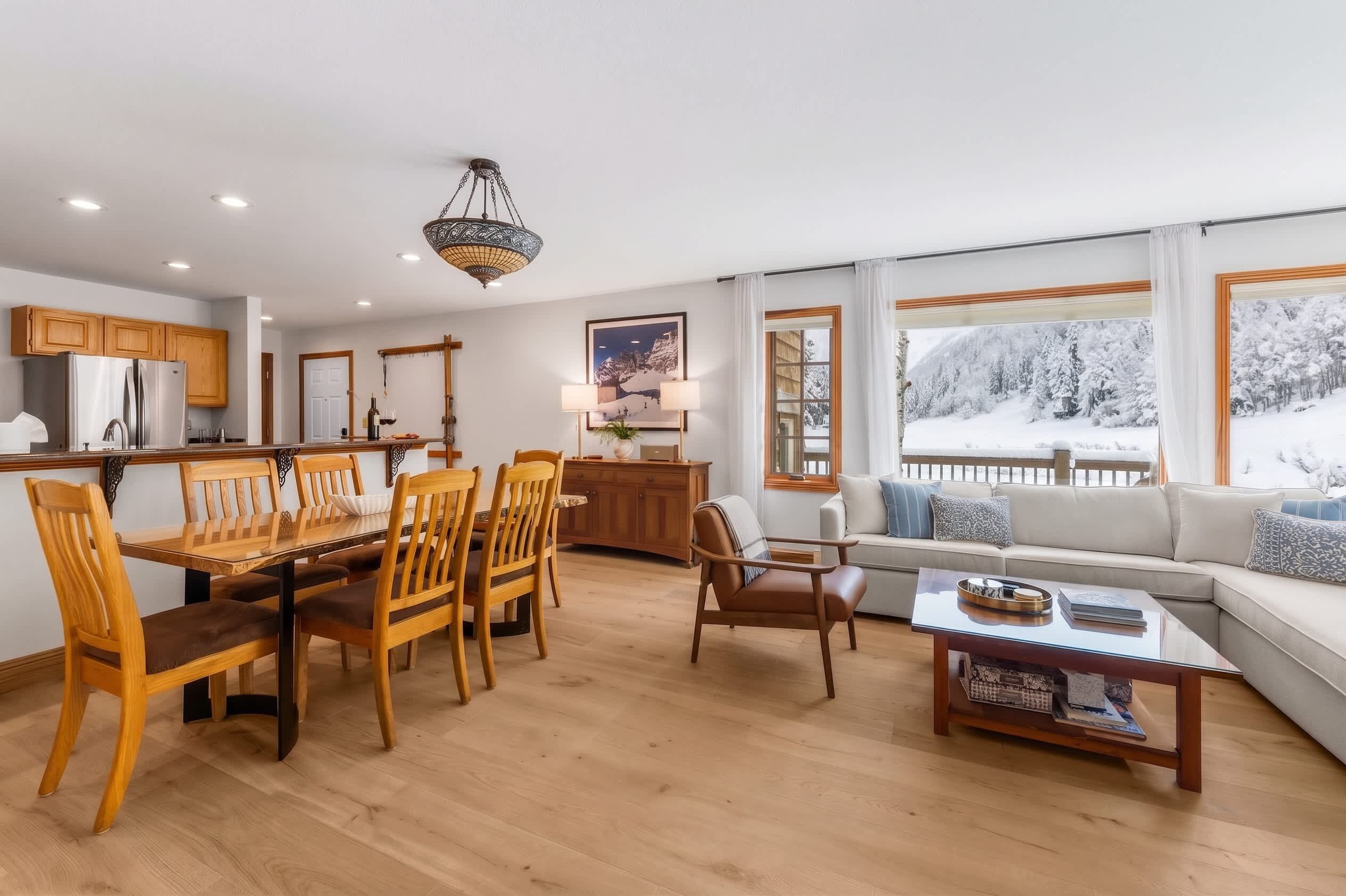 A modern kitchen with wooden cabinets, a stainless steel refrigerator, and a dining area with wooden chairs and a glass table.