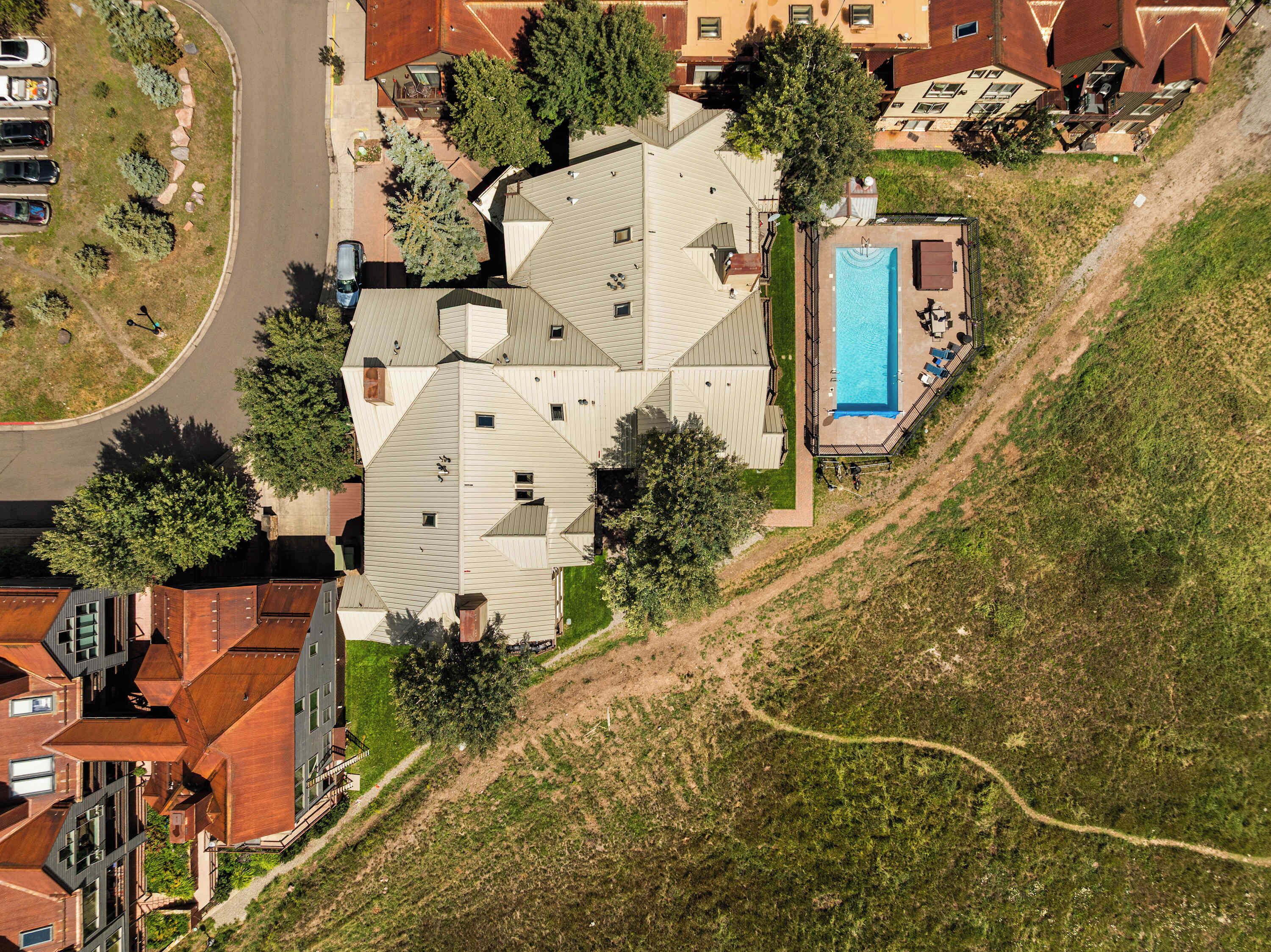 A residential area with a swimming pool, multiple houses, and a road.