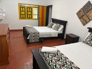 A hotel room with two beds, a wooden dresser, a small table, and a window with a colorful door. - Vrbo Property (rural)