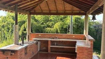 An outdoor barbecue area with a brick grill, a sink, and a covered roof.