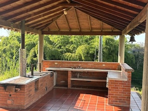 An outdoor barbecue area with a brick grill, a sink, and a covered roof. - Coffee farm 15 minutes from the coffee park (rural)